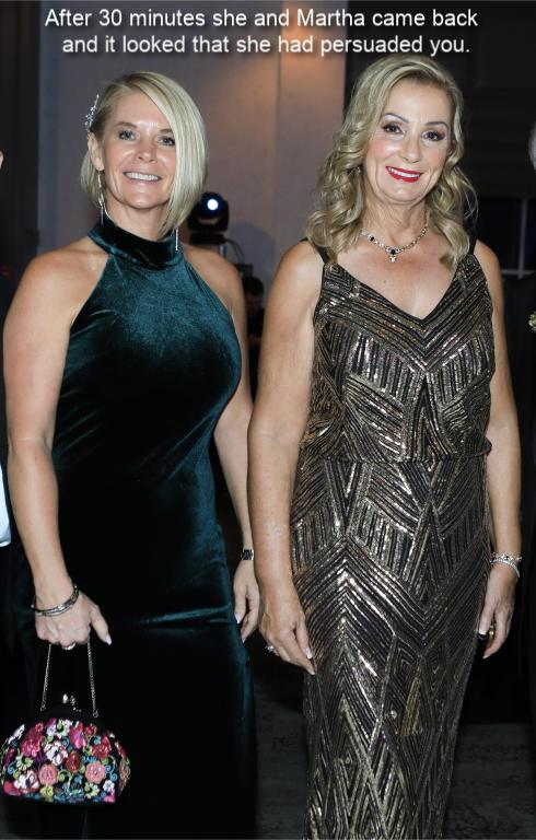 Two women standing together at an event, one in a green dress and the other in a sparkling gold dress, with elegant hairstyles and accessories.
